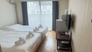 A hotel room with two beds, each with neatly folded towels. There is a desk with a lamp and a television on a stand. - DYNAST SHIBUYA NO.1 (Tokyo)