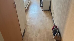 A narrow hallway with wooden flooring, a white cabinet, and a shoe rack with several pairs of shoes. - DYNAST SHIBUYA NO.1 (Tokyo)