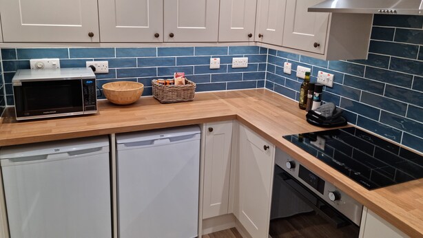 A modern kitchen with white cabinets, a microwave, a dishwasher, and a stove. - Bright 1 bedroom Apartment in Drymen (Drymen)