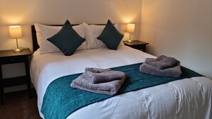 A neatly made bed with white linens, two green pillows, and a teal throw blanket. There are two bedside lamps on wooden nightstands. - Bright 1 bedroom Apartment in Drymen (Drymen)