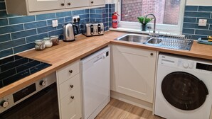 A modern kitchen with a dishwasher, a built-in oven, a sink, and a window overlooking a brick wall. - Bright 1 bedroom Apartment in Drymen (Drymen)