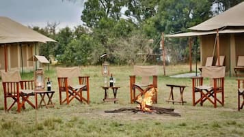 A campsite with tents, chairs, tables, and a central fire.