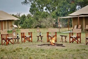 Un camping con tiendas de campaña, sillas, mesas y una fogata central.
