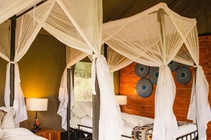 Habitación con cuatro camas, cada una con dosel. Hay lámparas de pared y una mesita con lámpara.