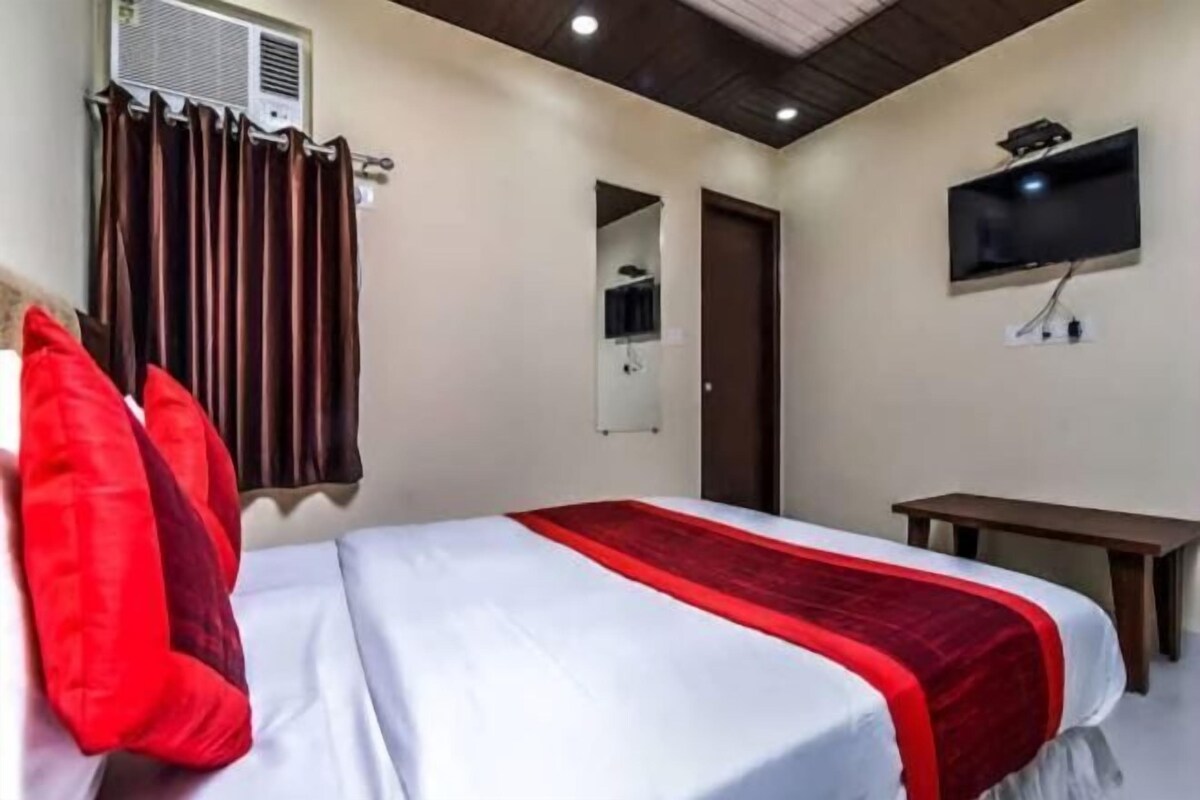 A hotel room with a bed, a TV, a desk, and an air conditioning unit.