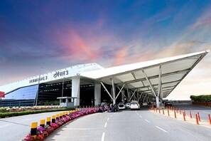 An airport terminal with a covered walkway, multiple lanes for vehicles, and a clear sky. - Hotel Swastik Stay (New Delhi)