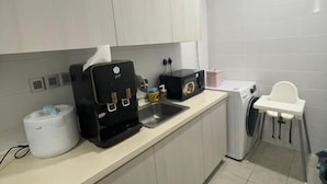 Une petite cuisine équipée d’une machine à café, d’un grille-pain, d’un évier et d’un lave-linge.