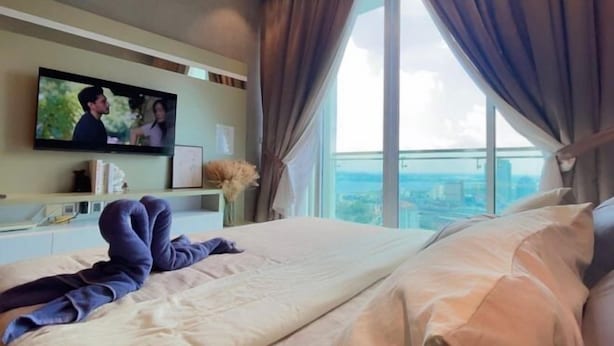 Une chambre d’hôtel avec un lit, un téléviseur fixé au mur, une fenêtre avec des rideaux et une vue sur le paysage urbain.