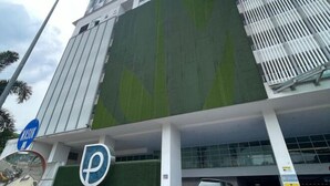 Un bâtiment moderne à la façade verdoyante, avec un panneau indiquant un parking et une entrée bien visible.