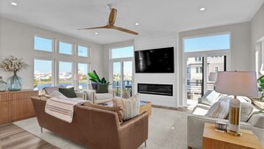 A modern living room with a brown sofa, a flat-screen TV, a fireplace, and large windows offering a view of the city.