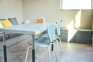 A dining area with a table and chairs, a sofa, and a window providing natural light. - TAITO ASAKURA STAY (Tokyo)
