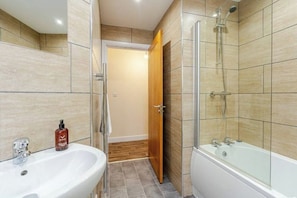 A bathroom with a sink, shower, and a wooden door leading to another room. - Cosy Modern Flat, Cockermouth, Sleeps 4 (Cockermouth)