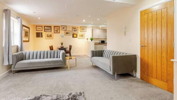 A living room with two sofas, a small table, and a kitchen in the background. - Cosy Modern Flat, Cockermouth, Sleeps 4 (Cockermouth)
