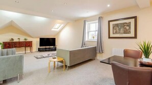 A modern living room with a sofa, a TV, a dining table, and a painting on the wall. - Cosy Modern Flat, Cockermouth, Sleeps 4 (Cockermouth)