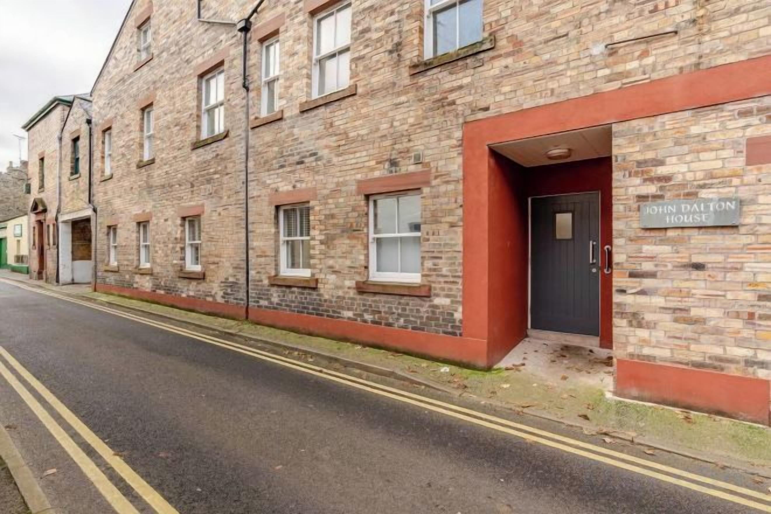 A brick building with a red-framed entrance and a sign reading 'John Dalton House.'