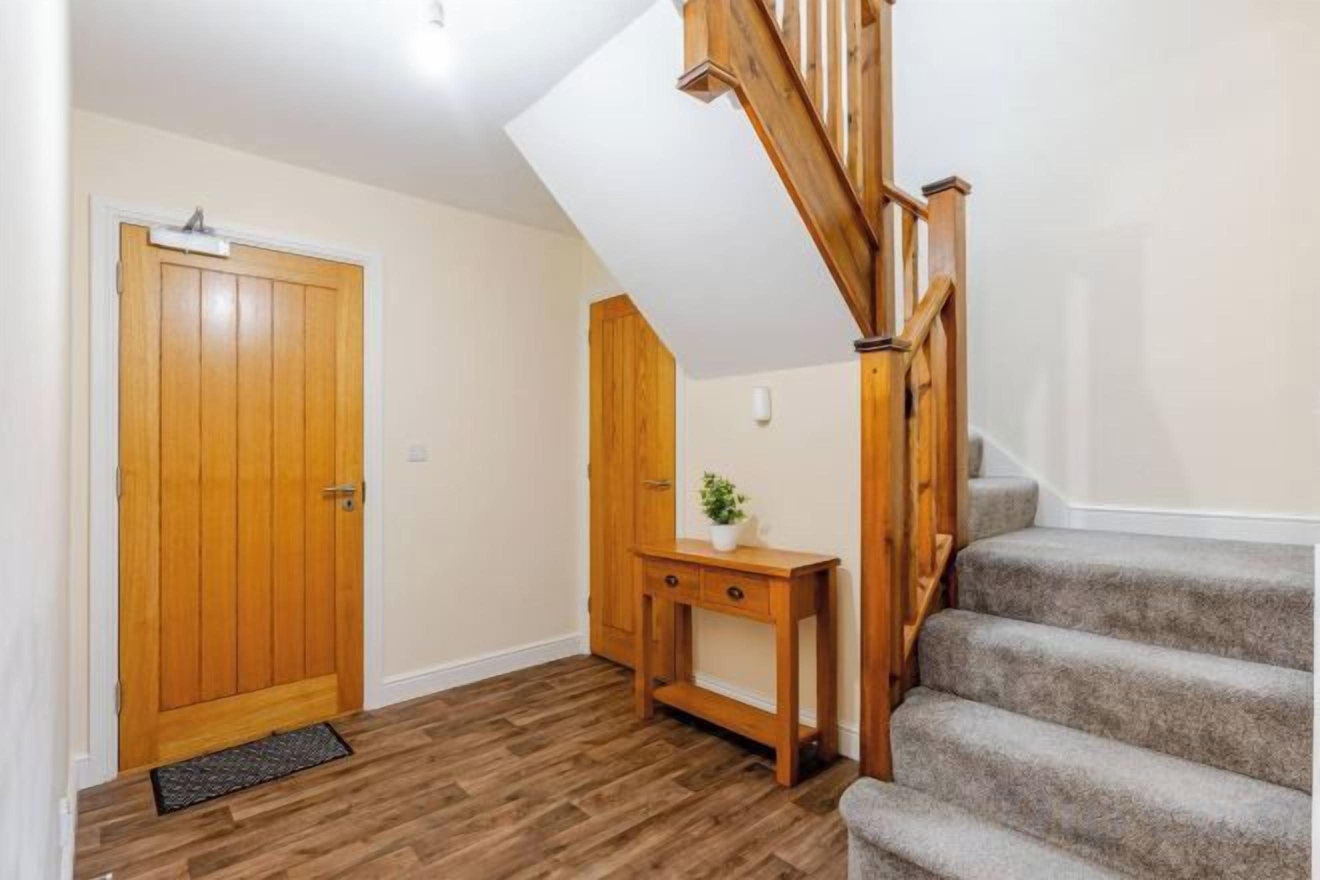 Una escalera con barandas de madera que lleva a una plataforma, una puerta de madera y una pequeña mesa de madera con una planta.