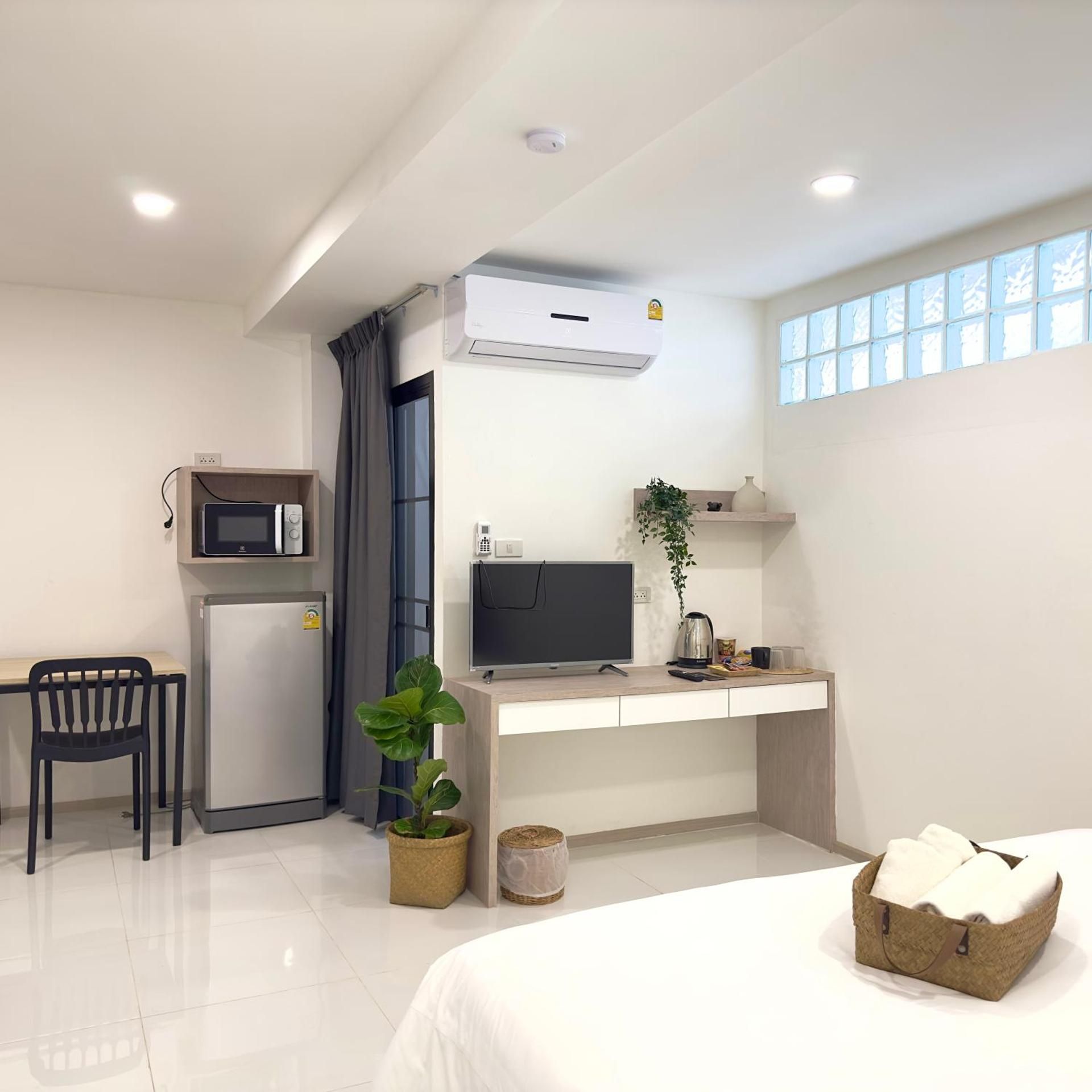 Habitación de hotel con cama, escritorio con computadora, refrigerador pequeño, televisión y ventana con cortinas.