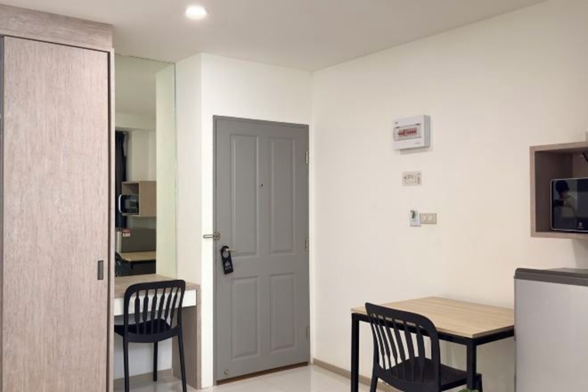 Une petite pièce propre, avec une armoire en bois, une porte grise, un mur blanc, une petite table avec une chaise et un téléviseur fixé au mur.