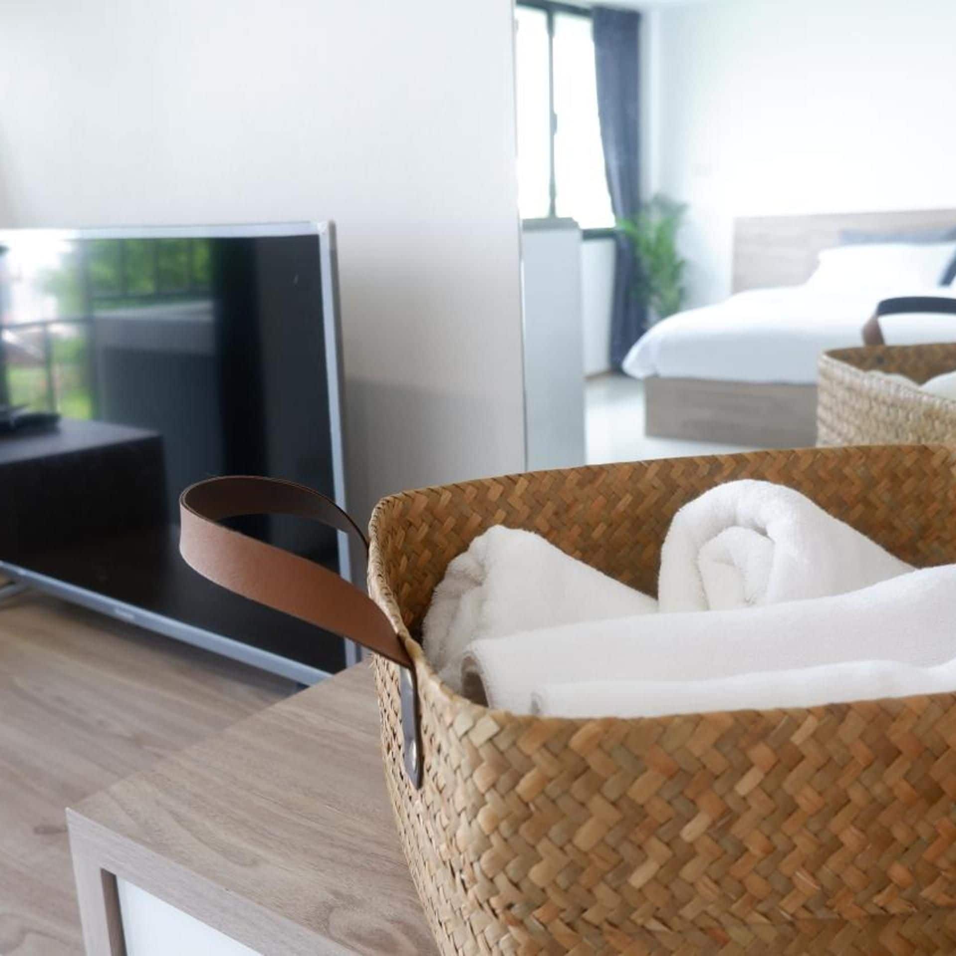 A woven basket with a handle on a wooden surface, likely a hotel room.