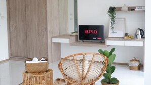 Een moderne woonkamer met een flatscreen waarop 'NETFLIX' staat, een rieten stoel, een klein tafeltje met een mand, en een potplant.