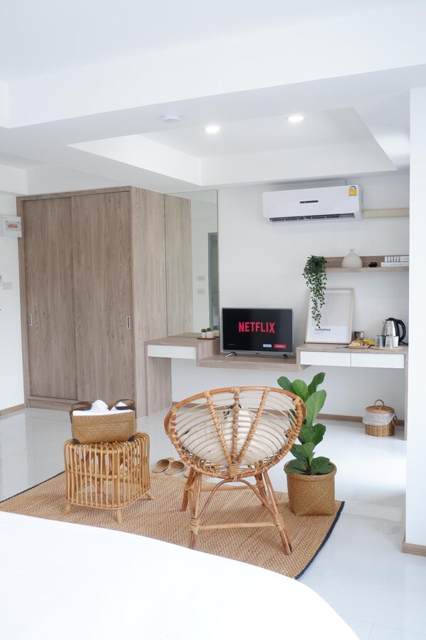 En moderne stue med et fladskærms-tv, der viser 'NETFLIX', en fletstol, et lille bord med en kurv og en potteplante.