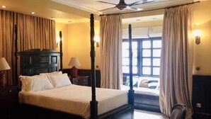 A four-poster bed with a headboard, two bedside tables with lamps, a ceiling fan, and a window with curtains. - Courtyard Pujan Hotel - Thamel (Kathmandu)
