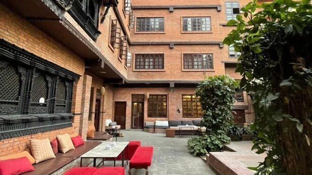 A courtyard with brick buildings, outdoor seating, and greenery. - Courtyard Pujan Hotel - Thamel (Kathmandu)