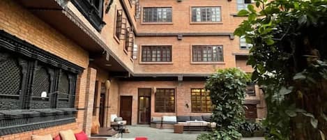 A courtyard with a brick building, outdoor seating, and greenery.