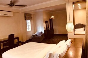 Une chambre d’hôtel comprenant un lit, un bureau, une chaise, une commode, un miroir et un luminaire suspendu.