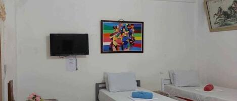 A room with two single beds, a television mounted on the wall, and a painting above one bed.
