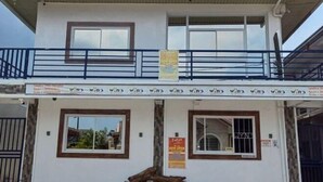 Un edificio di due piani con un balcone, un cartello che indica 'Ora Aperto' e una finestra vista sulla campagna circostante.