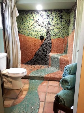A bathroom with a mosaic wall, a toilet, and a shower area.