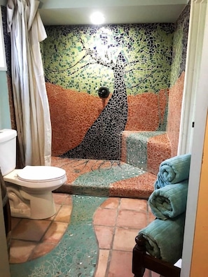 A bathroom with a mosaic wall, a toilet, and a shower area.