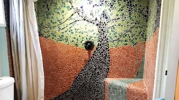 A bathroom with a mosaic wall, a toilet, and a shower area.