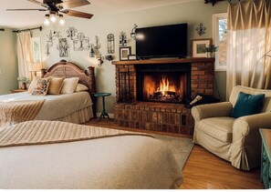 A cozy bedroom with a fireplace, a bed with a headboard, a television, and a ceiling fan.