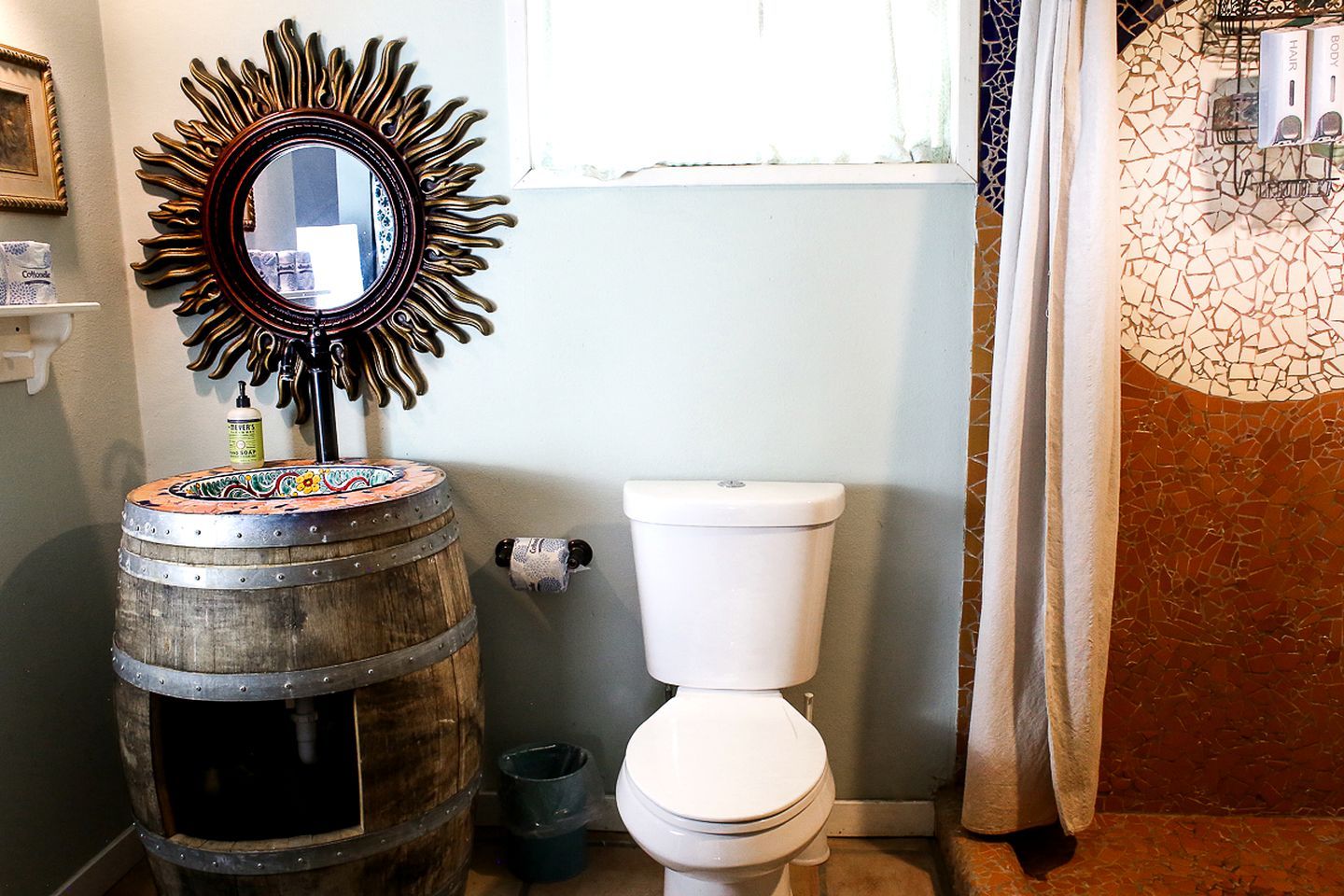A bathroom with a toilet, a decorative mirror, and a wooden barrel.