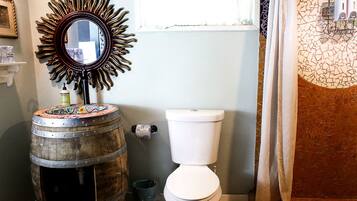 A bathroom with a toilet, a decorative mirror, and a wooden barrel.