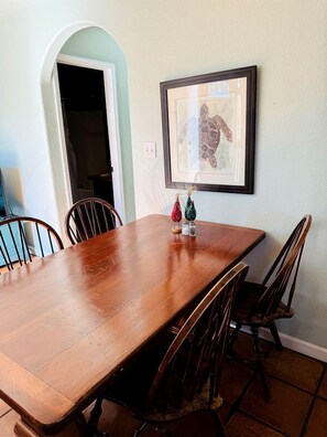 A dining room with a wooden table and chairs, a framed picture on the wall, and a doorway leading to another room.