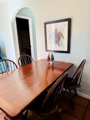 Une salle à manger avec une table et des chaises en bois, un tableau encadré au mur et une porte-fenêtre donnant sur une autre pièce.