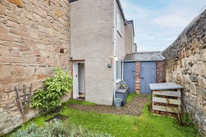 A narrow courtyard with a stone wall, a wooden door, and a small shed. - Host & Stay | The Reading Room (Hexham)