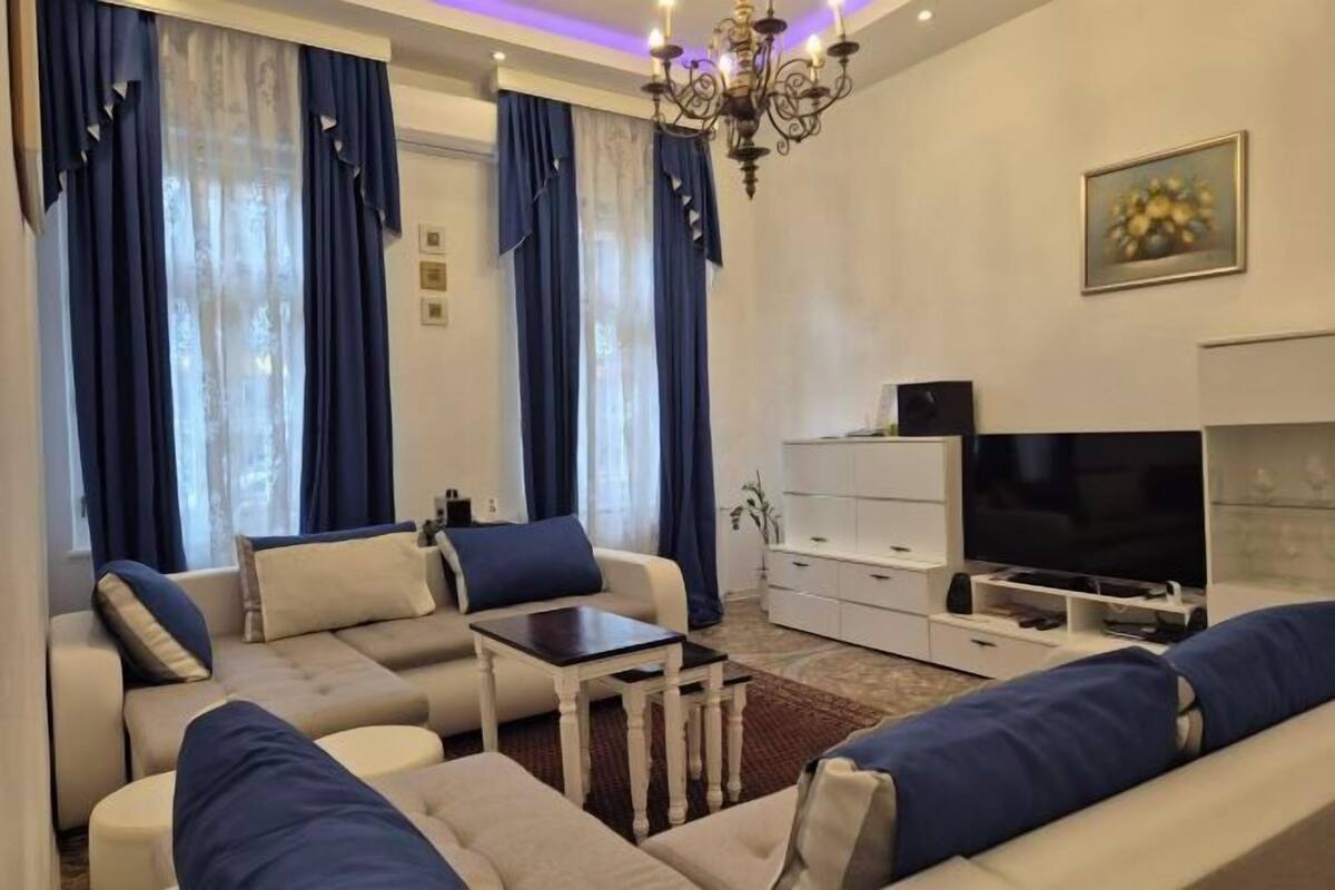 A living room with a sofa set, a TV, a white cabinet, and a chandelier.