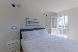A bedroom with a bed, a nightstand, a painting, and a door leading to an outdoor area.