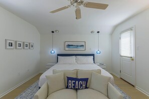 Une chambre à coucher comprenant un lit, un ventilateur de plafond, une table de chevet, des lampes fixées au mur, une porte et des tableaux encadrés.