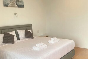 A neatly made bed with pillows and folded towels, a headboard, and a wall-mounted light fixture. - Sichon Residence (Sichon)