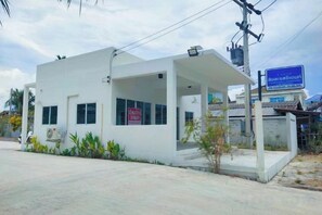 A white building with a covered entrance, a signboard, and a blue sign in the background. - Sichon Residence (Sichon)