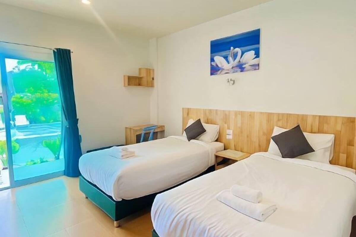 Une chambre d’hôtel avec deux lits, une tête de lit en bois, un tableau et une vue sur la verdure, visible à travers une porte coulissante.