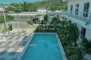 Una piscina en la azotea con suelo a cuadros, rodeada de palmeras y vistas a un edificio.
