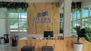 A reception desk with a wooden finish, a monitor, and a plant. - Sichon Residence (Sichon)