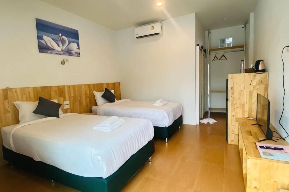 Une chambre d’hôtel avec deux lits, des têtes de lit en bois, du linge de lit blanc, un bureau en bois et un climatiseur fixé au mur.