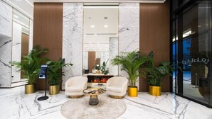 A lobby with marble flooring, two white armchairs, a round coffee table, and potted plants.